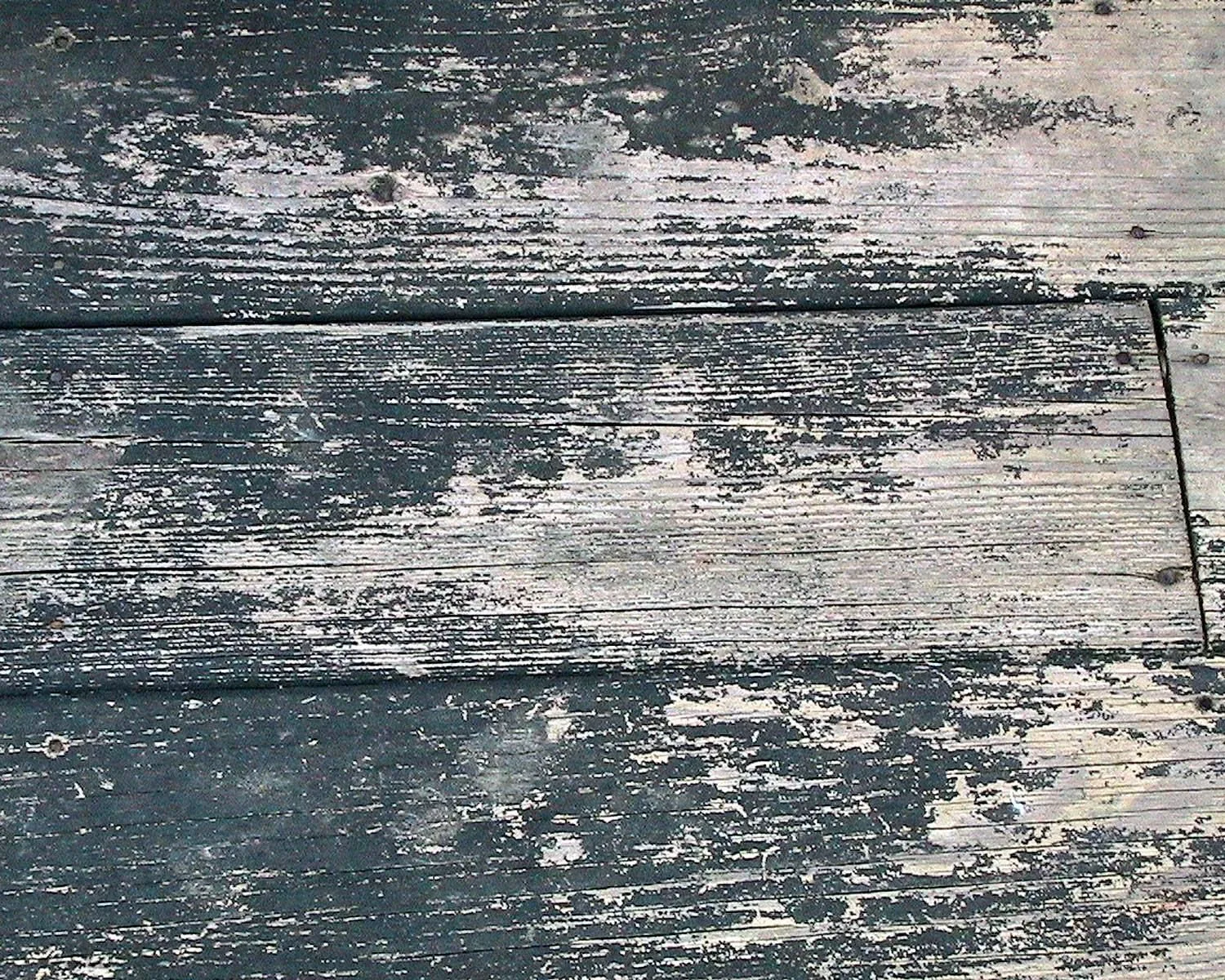 Old deck boards with dark paint flaking away from the grain